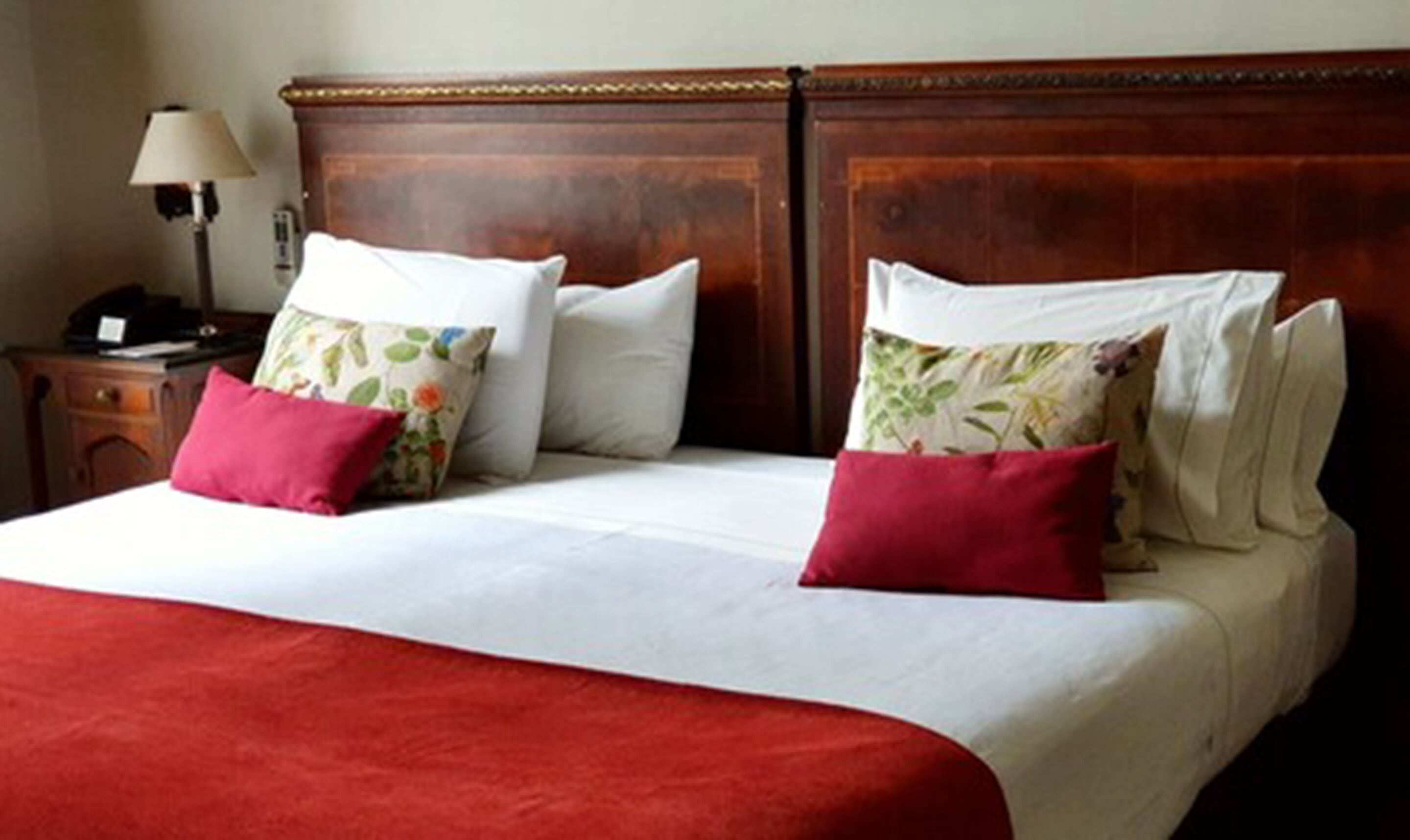 A neatly made bed with a red blanket, white pillows, and floral-patterned pillows.