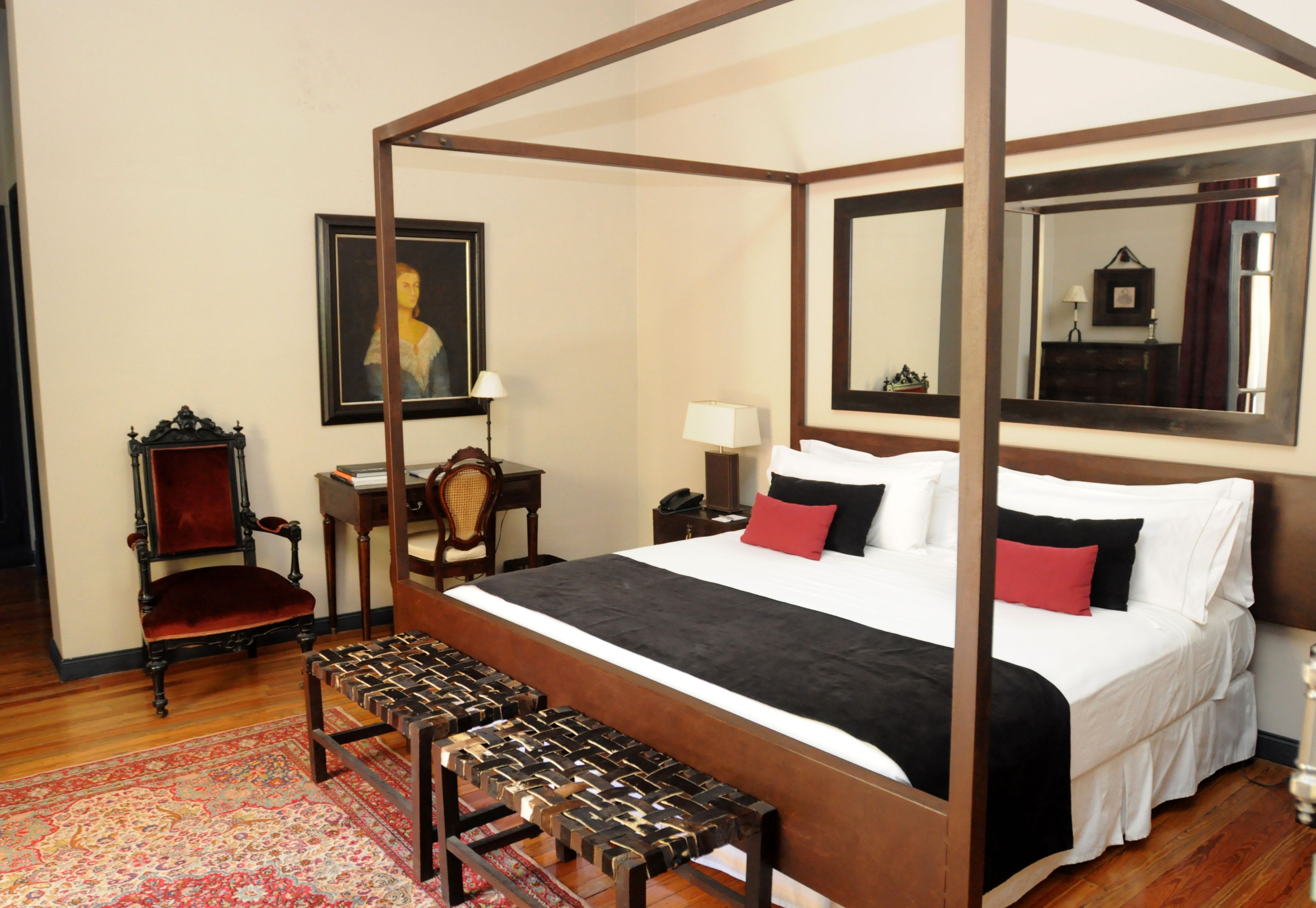 A four-poster bed with a canopy, a red and black bedspread, and a wooden bench at the foot of the bed.