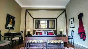 A four-poster bed with a mirror above, a desk with a chair, a bench, and a patterned rug.