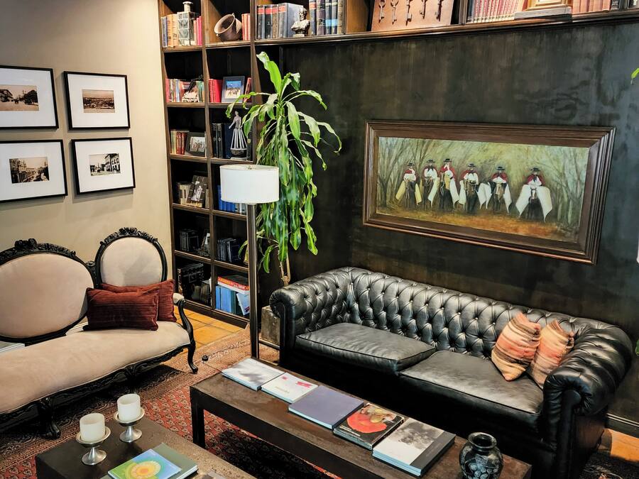 A cozy living room with a leather sofa, a coffee table with books, a bookshelf filled with books and decorative items, and a framed painting on the wall.