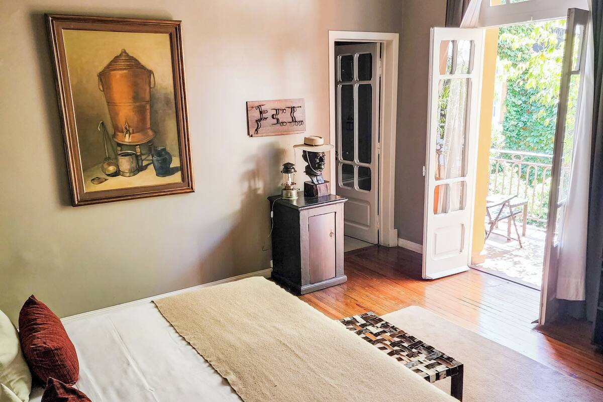 A bedroom with a bed, a painting, a dresser, and a door leading to an outdoor area.