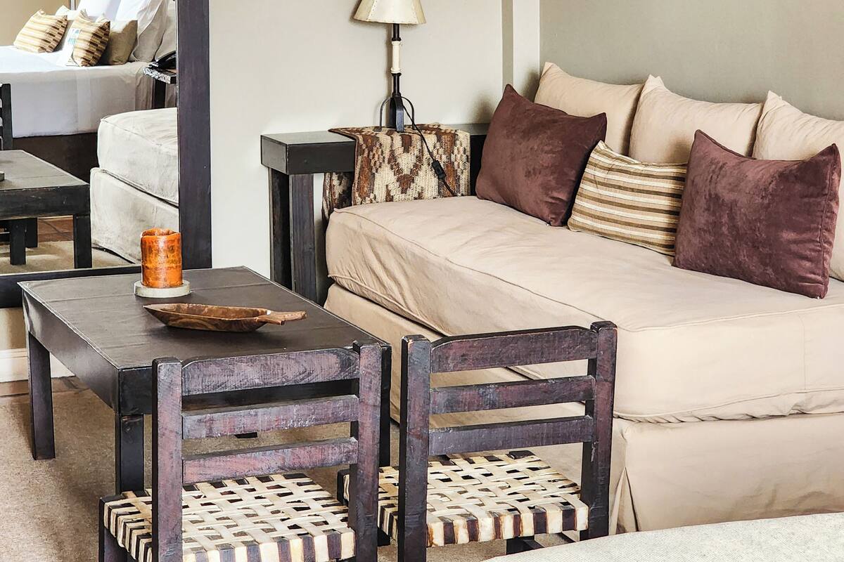 A cozy hotel room with a sofa, two chairs, a table with a candle, and a lamp.