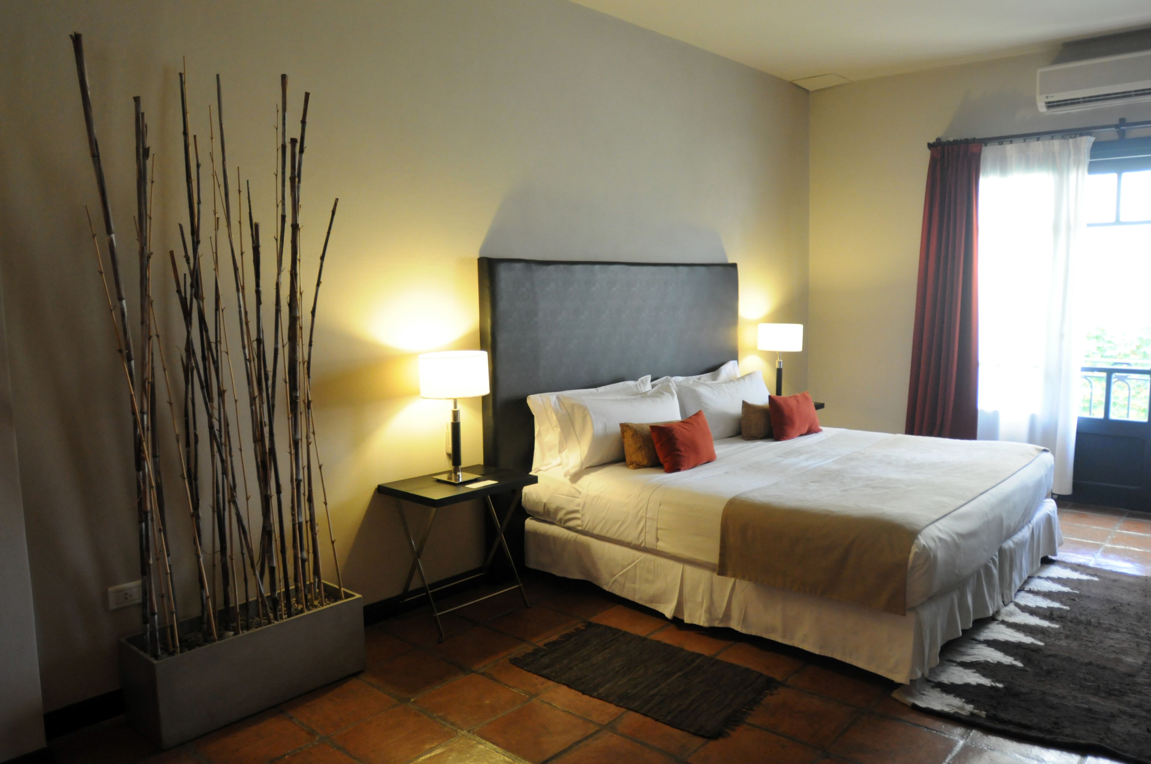 Un dormitorio ordenado con una cama grande, lámparas de noche, una mesita y una planta decorativa.