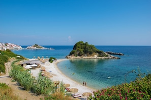 Una playa costera con aguas cristalinas, una pequeña isla y algunas sombrillas.
