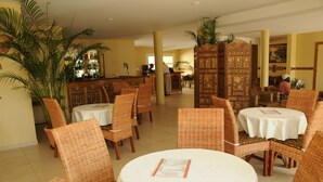 Un restaurant avec des chaises en osier et des tables rondes, un coin bar et un comptoir d’accueil.