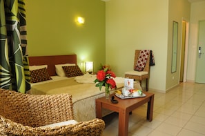 Quarto de hotel com uma cama, área de estar com uma poltrona, uma mesinha com bandeja de itens de café da manhã e um porta-toalhas fixado na parede.
