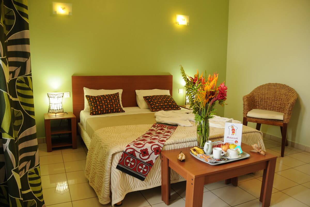 Une chambre d’hôtel comprenant un lit, des tables de chevet, une chaise, une table avec des articles pour le petit-déjeuner et un vase de fleurs.