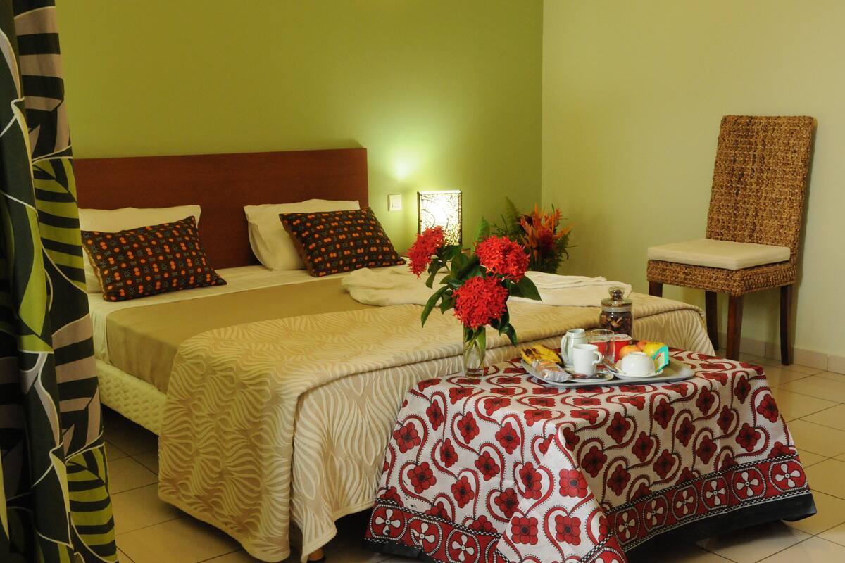 Une chambre d'hôtel avec un lit, une chaise, une table sur laquelle se trouve un plateau avec des articles pour le petit-déjeuner, et un vase rempli de fleurs.