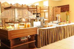 Uma mesa de buffet com estação de café, exposição de frutas e diversos alimentos.