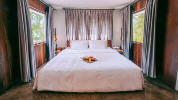 A large, neatly made bed with a white bedspread and pillows, positioned in a room with wooden walls and large windows.
