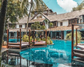 A pool area with thatched-roof structures, lounge chairs, and tropical plants. - Villa Samadhi by Samadhi (Kuala Lumpur)