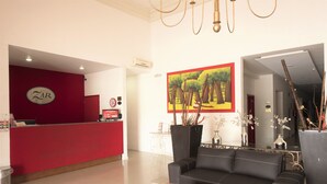 Un área de recepción con un escritorio rojo, un sofá negro y un cuadro con árboles.