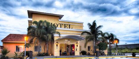 A hotel with a parking lot, palm trees, and a clear sky.