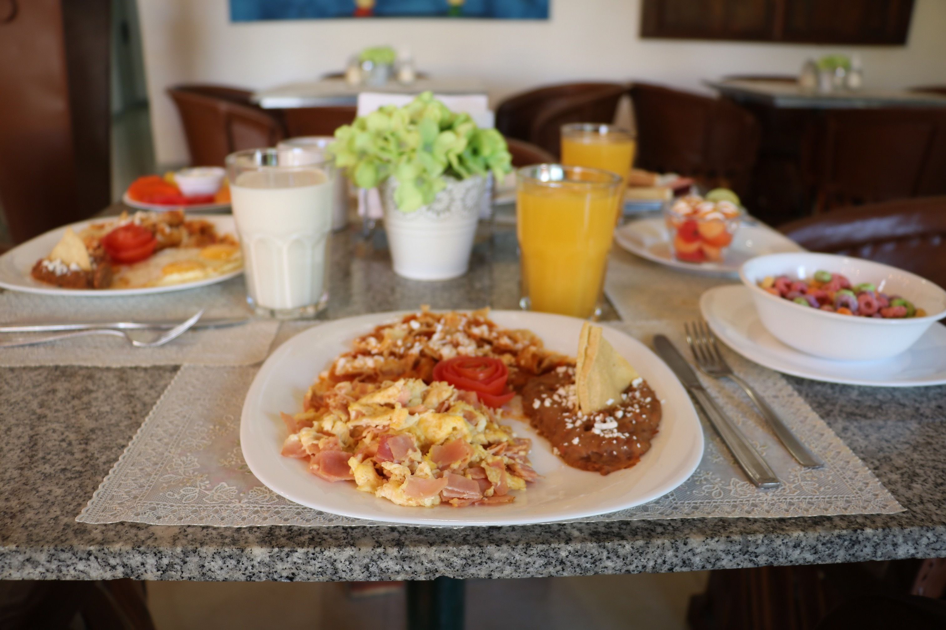 A breakfast table with plates of food, a glass of orange juice, and a bowl of fruit.
