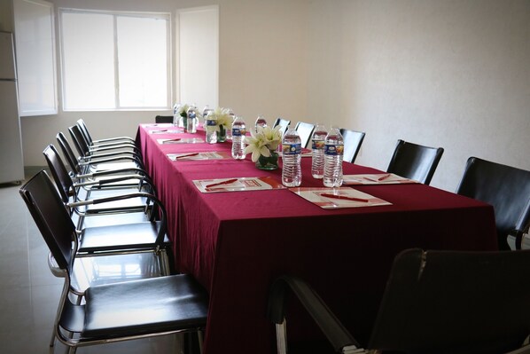 Un salón de conferencias con una larga mesa, sillas, botellas de agua y arreglos florales.