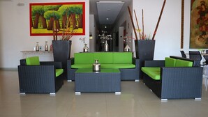 Un vestíbulo con un sofá verde, muebles de mimbre negros y dos jarrones grandes con plantas.