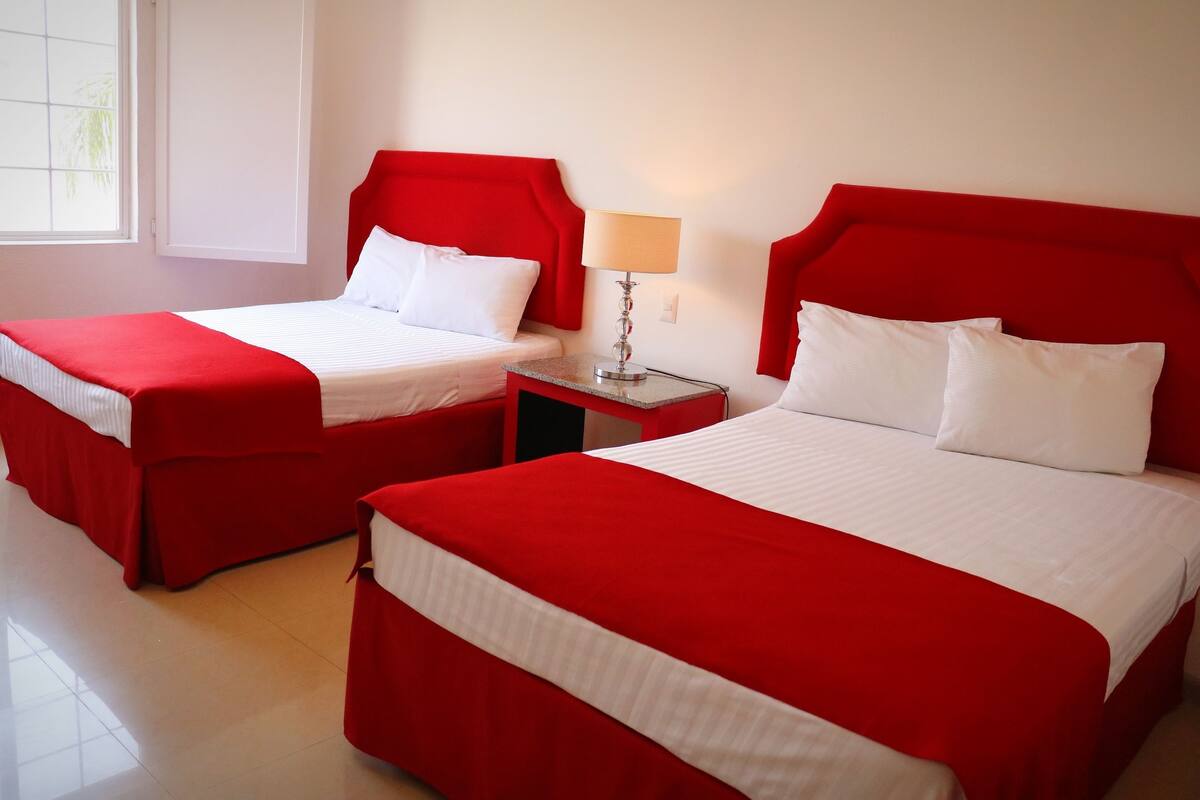 Dos camas rojas con sábanas blancas en una habitación de hotel.