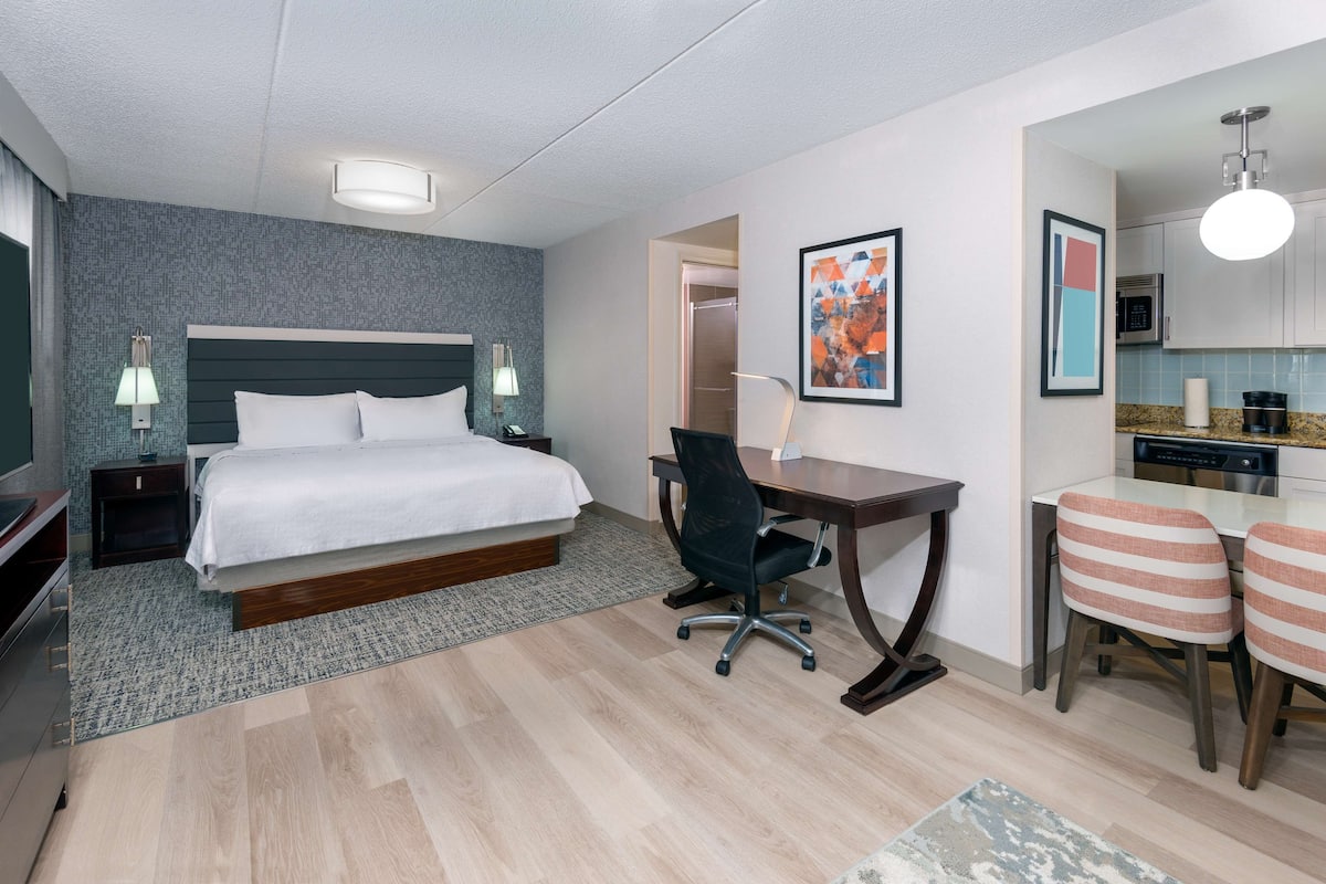 A hotel room with a bed, desk, office chair, and kitchenette.