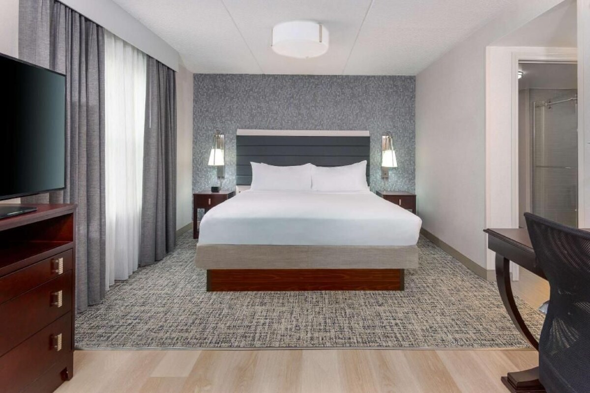 A hotel room with a large bed, a TV, a desk, and a chair.