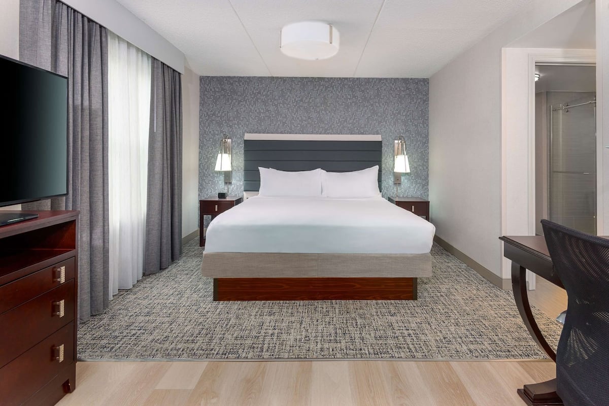 A hotel room with a large bed, a TV, a desk, and a chair.