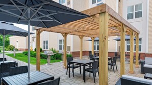 An outdoor patio with tables and chairs, a wooden pergola, and a barbecue grill. - Homewood Suites by Hilton Boston/Canton, MA (Canton)