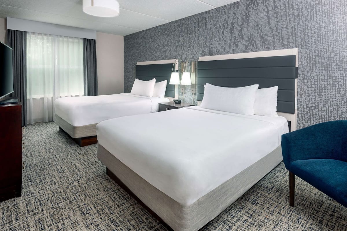 A hotel room with two beds, a TV, a desk, and a chair.