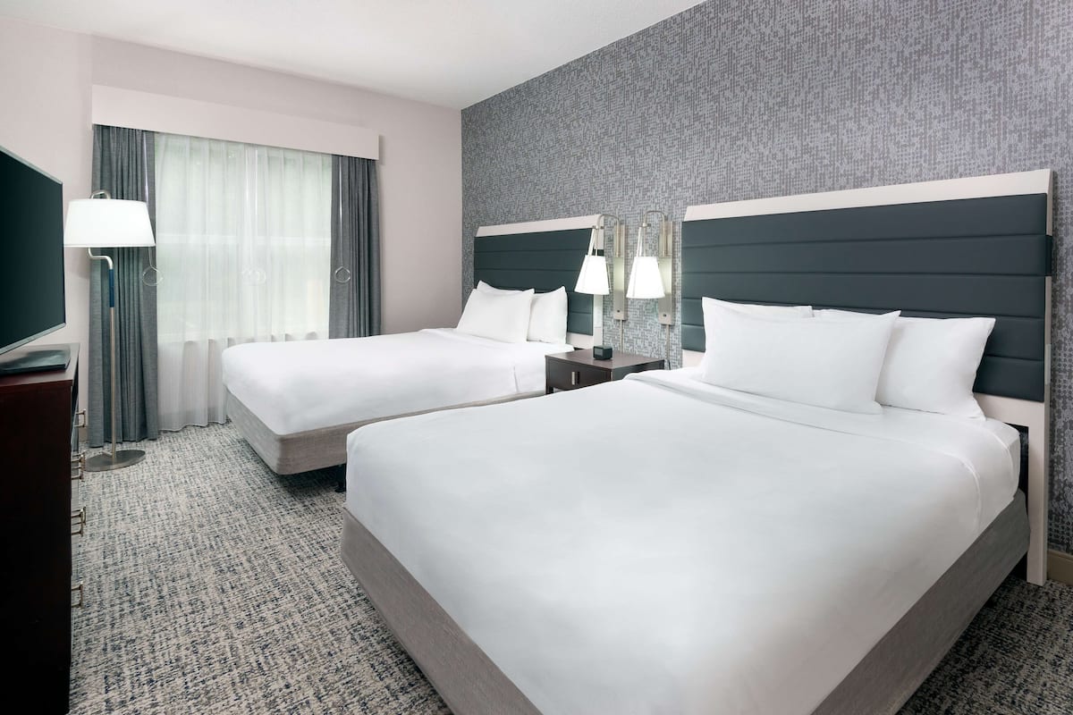 A hotel room with two beds, a TV, a desk, and a lamp.
