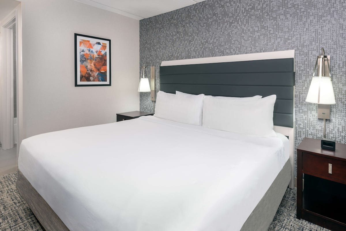 A neatly made bed with a dark headboard, two bedside tables with lamps, a framed picture on the wall, and a patterned carpet.