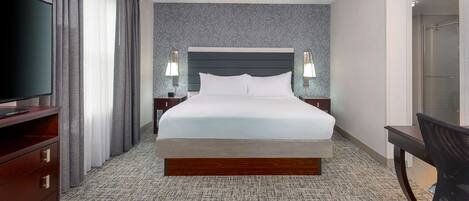 A hotel room with a large bed, a TV, a desk, and a chair.