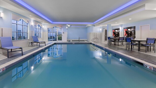 A modern indoor pool area with clear blue water, lounge chairs, and a seating area with tables and chairs. - Homewood Suites by Hilton Boston/Canton, MA (Canton)
