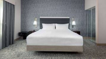 Una cama grande con cabecera oscura, dos mesitas de noche con lámparas, pared con textura y suelo alfombrado.