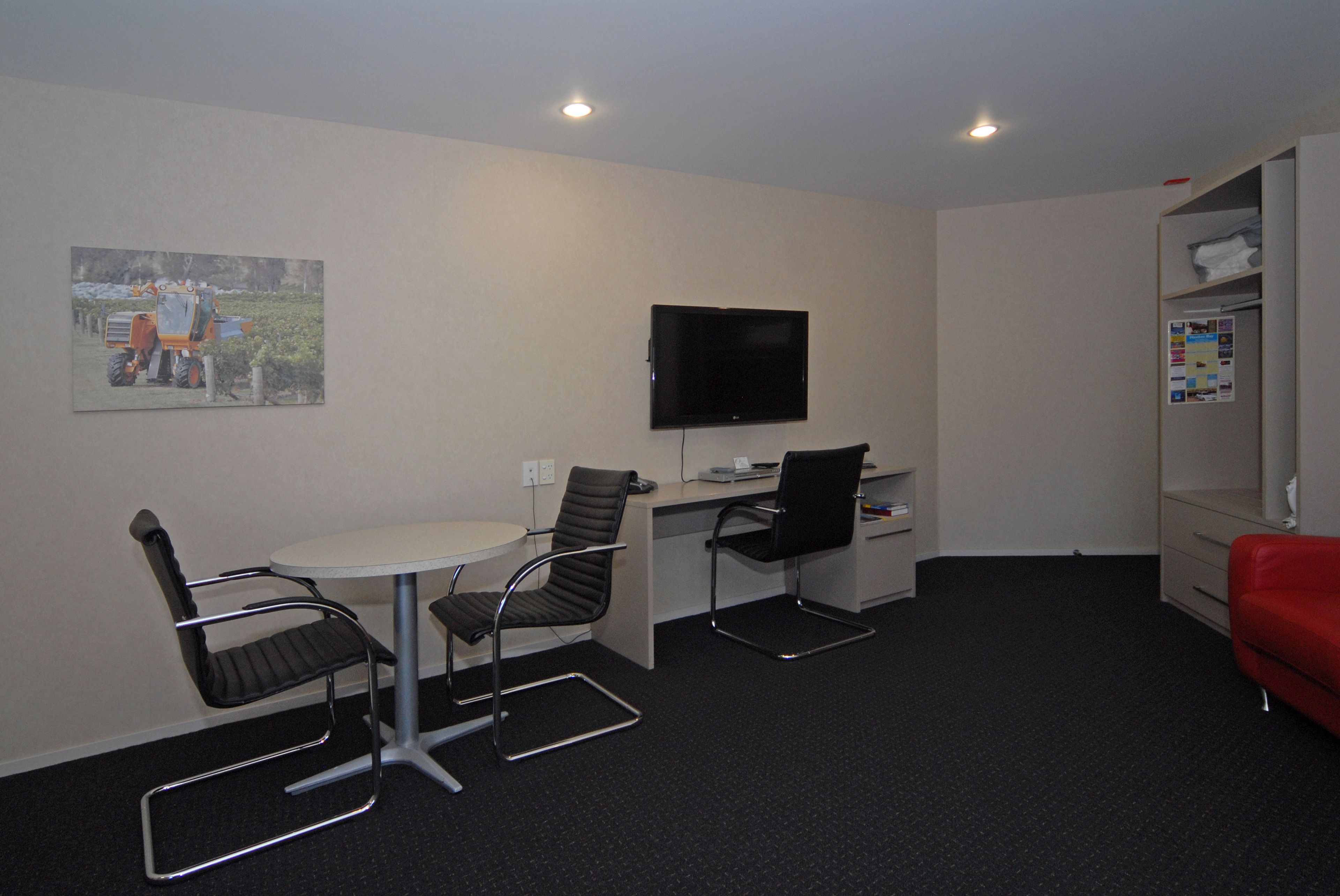 A small, modern office space with a desk, two chairs, a flat-screen TV, and a red sofa.