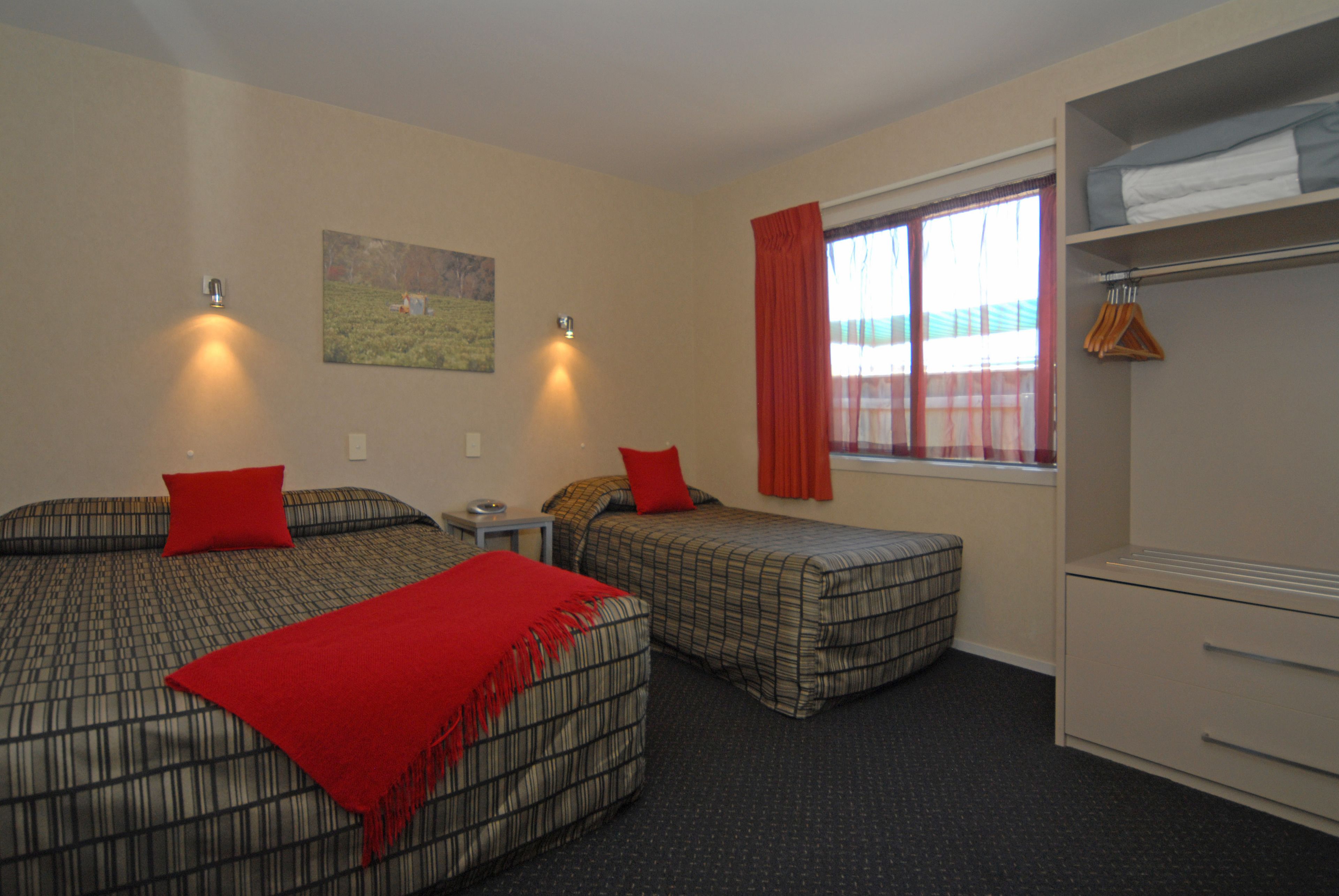 A hotel room with two beds, a desk, a window with curtains, and a wardrobe.