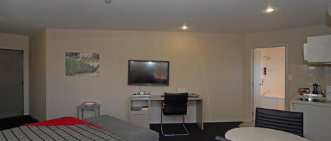 Habitación de hotel con cama, escritorio, silla, televisor, una mesita y kitchenette.