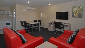 Una habitación de hotel moderna con sofás de cuero rojo, una mesa de comedor con sillas, un televisor de pantalla plana y una zona de cocina con microondas.