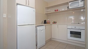Cocina compacta con electrodomésticos blancos, que incluyen un refrigerador, lavavajillas, microondas y horno.