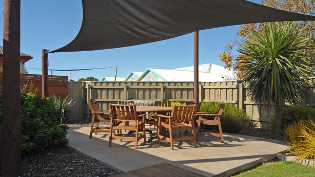 Un patio con una mesa y sillas de madera, rodeado por una valla de madera y plantas.