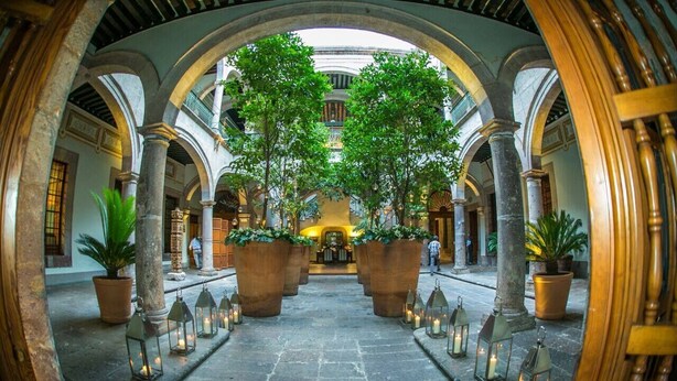 Un patio interior con zona de estar central, rodeado de columnas y macetas con plantas.