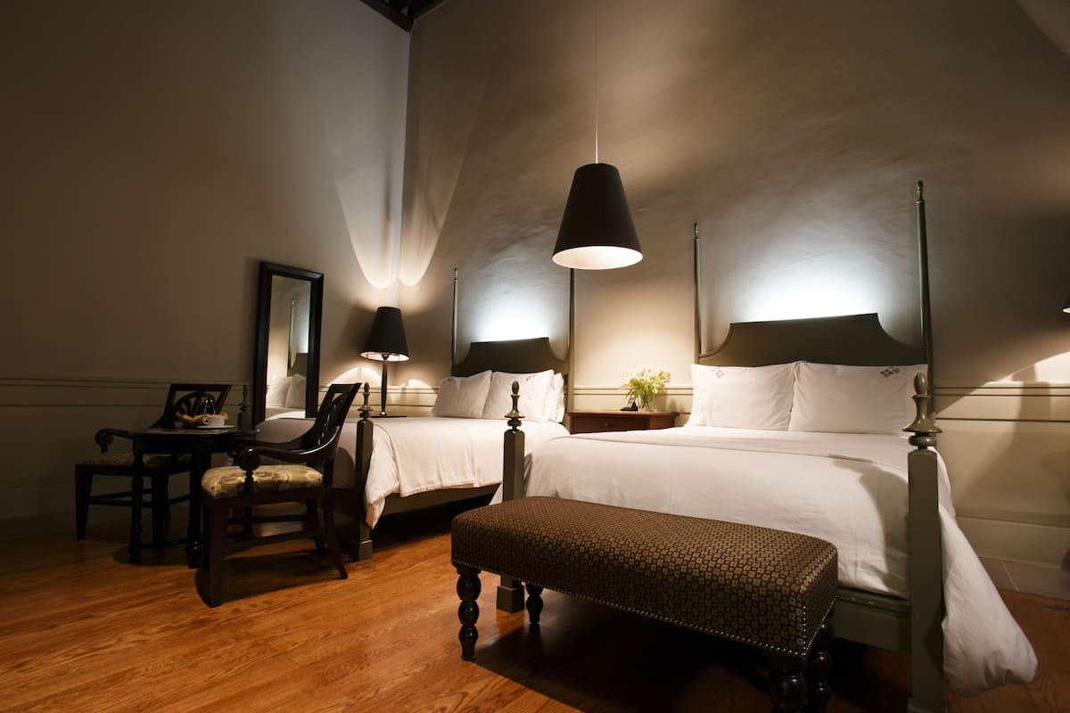 Habitación de hotel con dos camas, un banco, un escritorio con una silla y dos lámparas de noche.