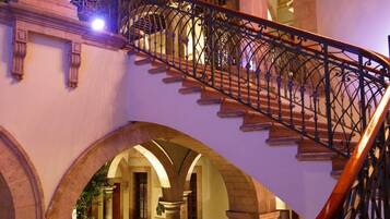 A grand staircase with ornate metal railings and stone balustrades, leading to an upper level with arched doorways and columns.
