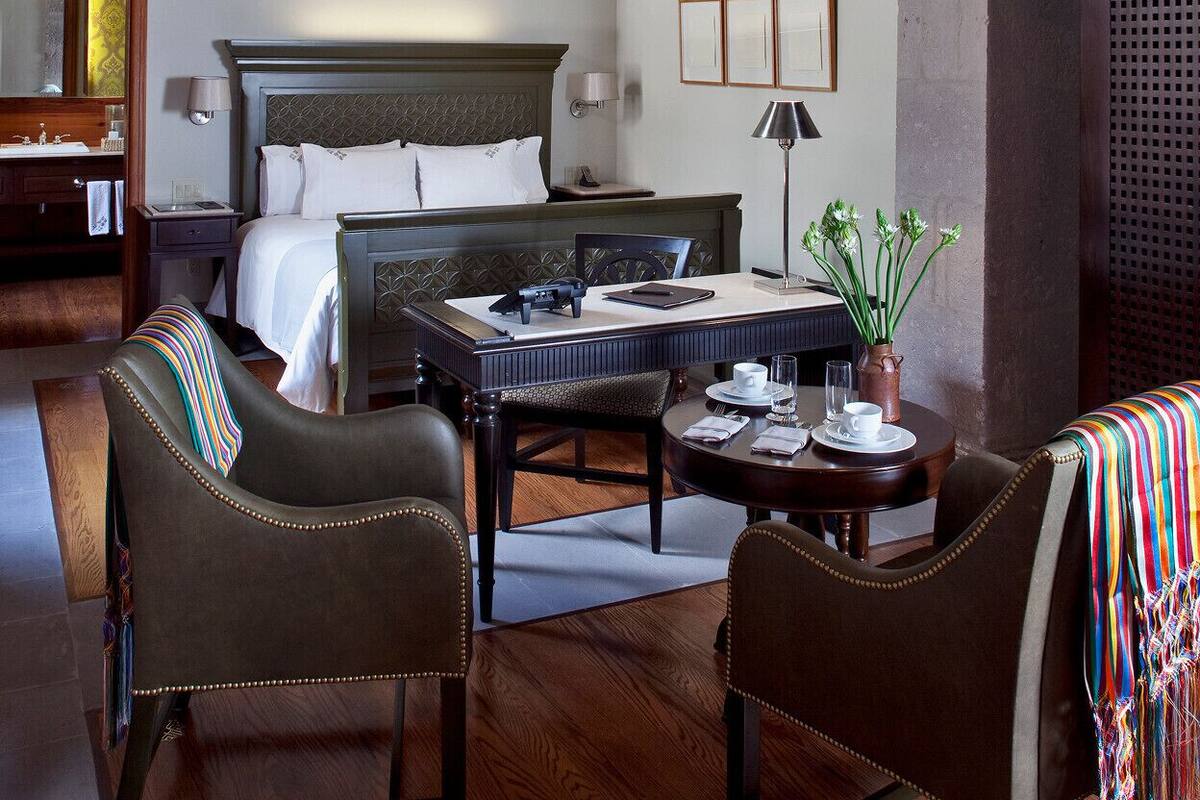Habitación de hotel con una cama, dos sillones, una mesita y una gran estructura de piedra en arco.
