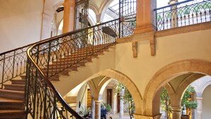 Una imponente escalera con barandillas de metal ornamentadas, varios arcos y una lámpara decorativa en el techo.