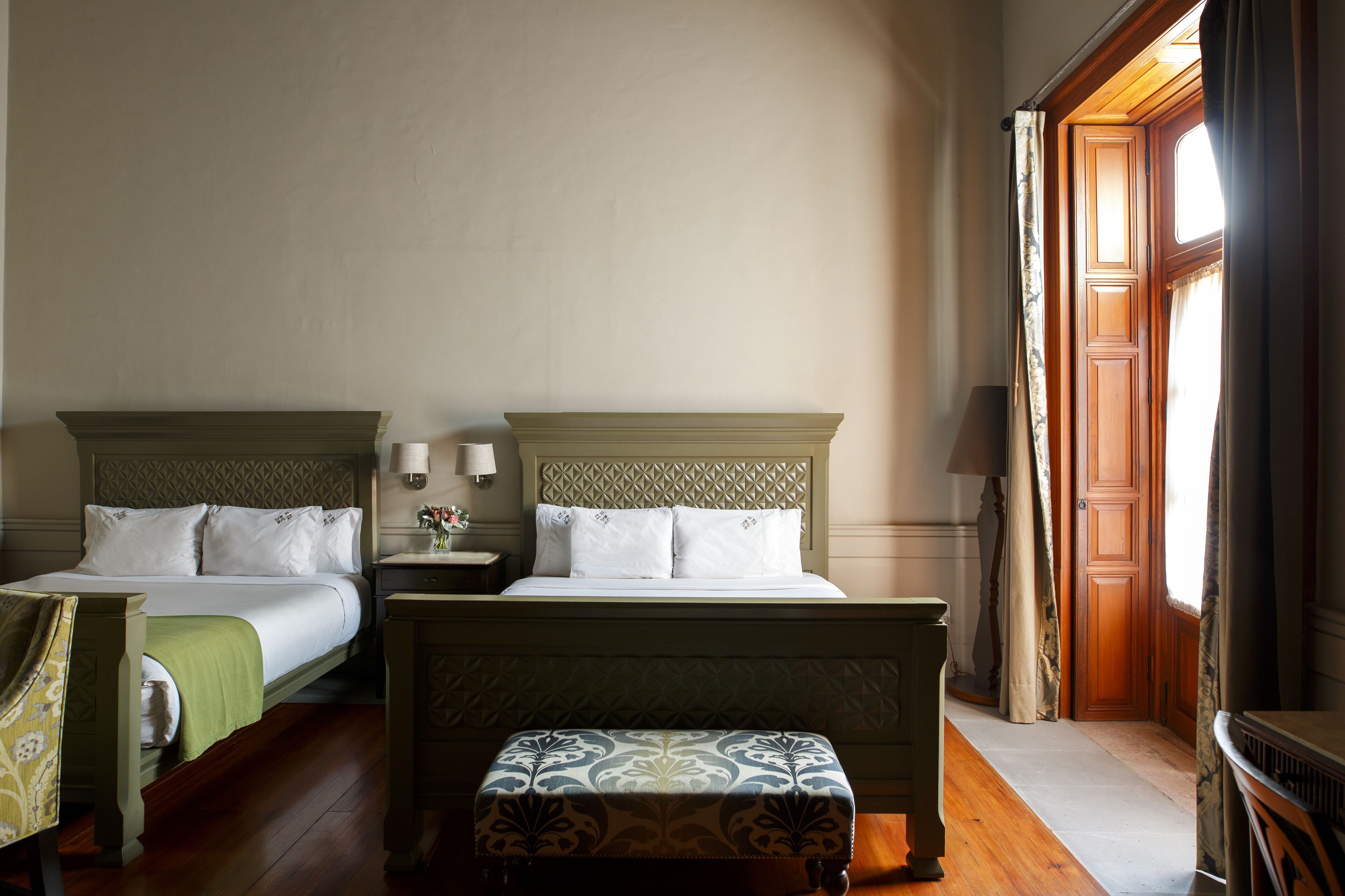 Una camera d'albergo con due letti, un comodino, una lampada e una finestra con tende.