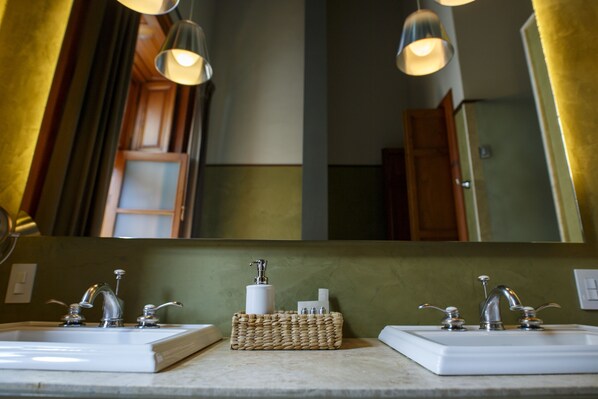 Un baño con dos lavamanos, un espejo y una cesta de mimbre con artículos de aseo.