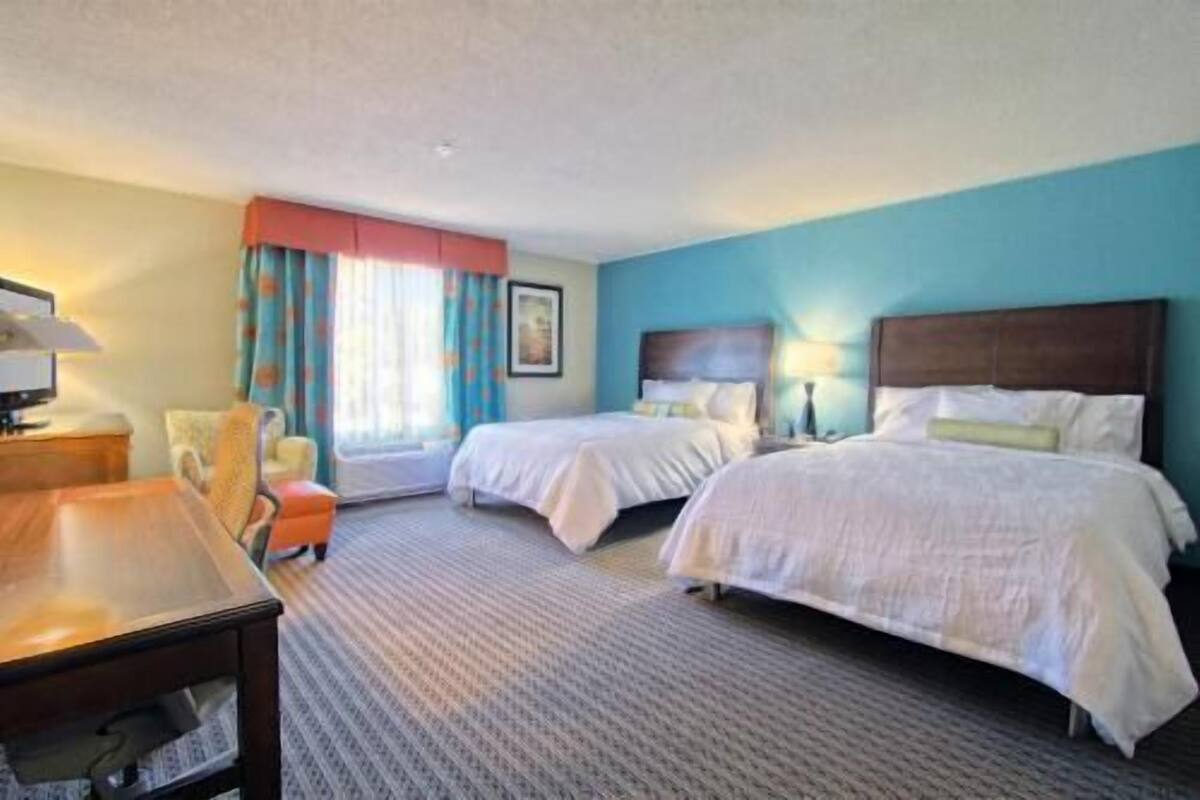 A hotel room with two beds, a desk, a chair, and a window with curtains.