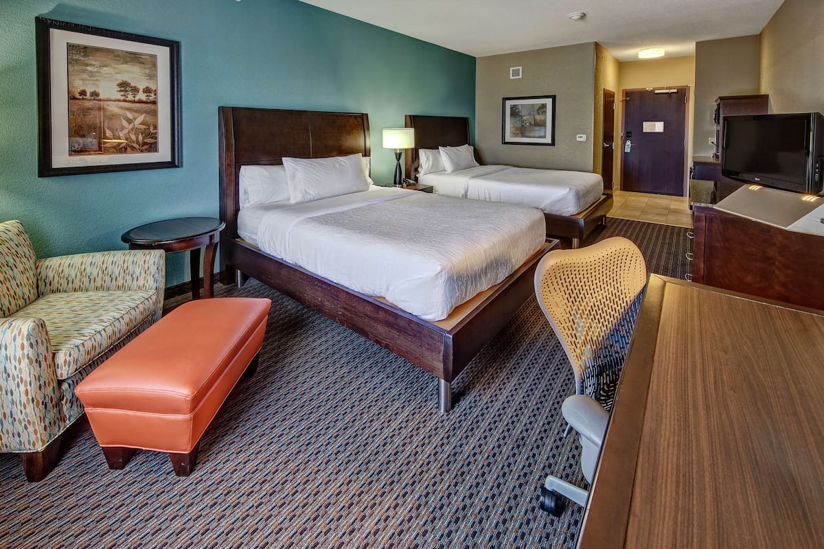 A hotel room with two beds, a sofa, a chair, a desk, and a TV.