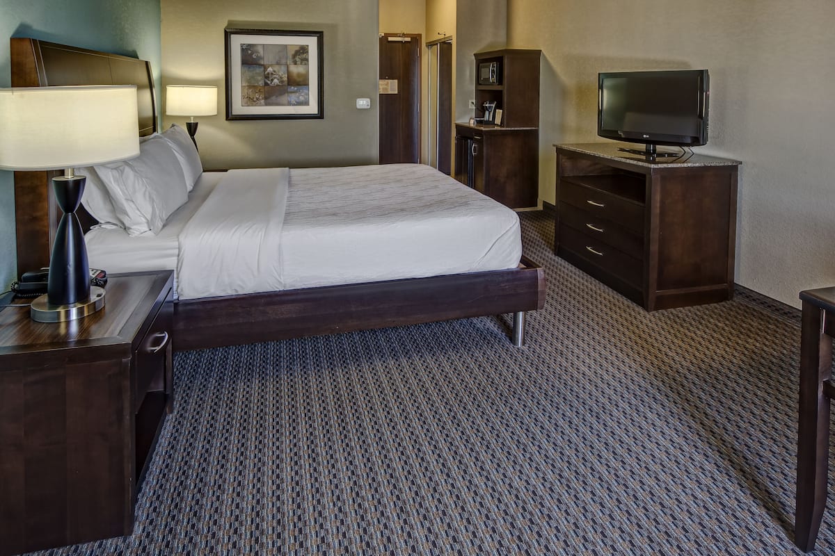 A hotel room with a bed, a desk with a lamp, a television on a stand, and a wardrobe.