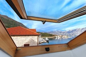 A room with a view of a lake, mountains, and a red-roofed building.