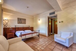 A hotel room with a bed, bedside table, lamp, chair, and a door leading to another room.