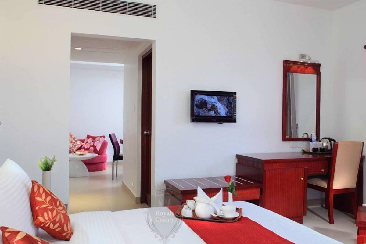 A hotel room with a bed, a desk, a chair, a television, and a bathroom visible through an open door.